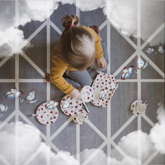 Young girl sitting on a playmat having an imaginary tea party with cloud and butterfly effects